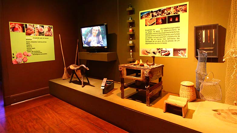 Interior do Museu do Folclore, mostrando objetos que estão em exposição, e vídeo reproduzido em TV